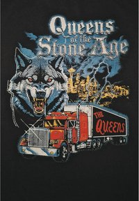 Sort t-shirt med et grafisk motiv af en uartig ulv med røde øjne og en stor rød lastbil, der tydeligt viser "THE QUEENS".