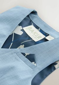 Šviesiai mėlyna liemenė su tekstūruotu audimu, gilus V formos iškirptė ir kišenė. Viduje tamsiai mėlynas gėlių raštas ir etiketė.