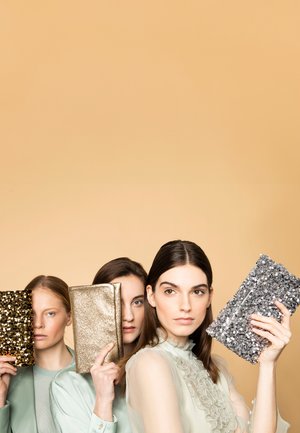 Three clutch bags: one covered in gold sequins, another in gold metallic fabric, and a third with silver sequins, held by three women.