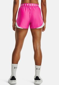 Rosa träningsshorts med vit trim, elastisk midja med texten "RUN", slätt tyg och design med rundad nederkant. Vita strumpor och svarta skor synliga.