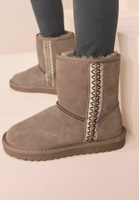 Botas de tobillo de ante gris con un acabado texturizado, que presentan costuras decorativas y acentos de cuentas a lo largo del costado, suela plana e interior suave.