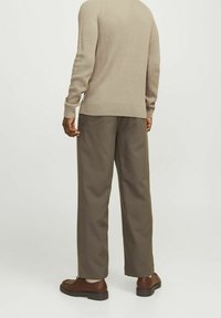 Maglione lavorato a maglia beige con texture a coste, abbinato a pantaloni marroni larghi e scarpe marroni stringate, visto da dietro.