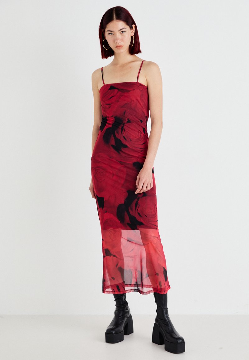 Vestido midi floral vermelho com alças finas, sobreposição transparente e padrão de rosas pretas. Combinado com botas de salto alto pretas. Textura suave.