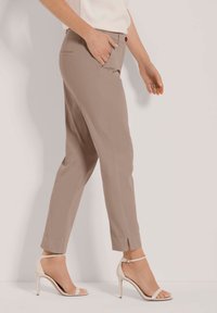 Beige slim-fit broek met zijzakken en omslagen, gedragen met lichtgekleurde hakken. Glad stof, op maat gemaakte ontwerp.