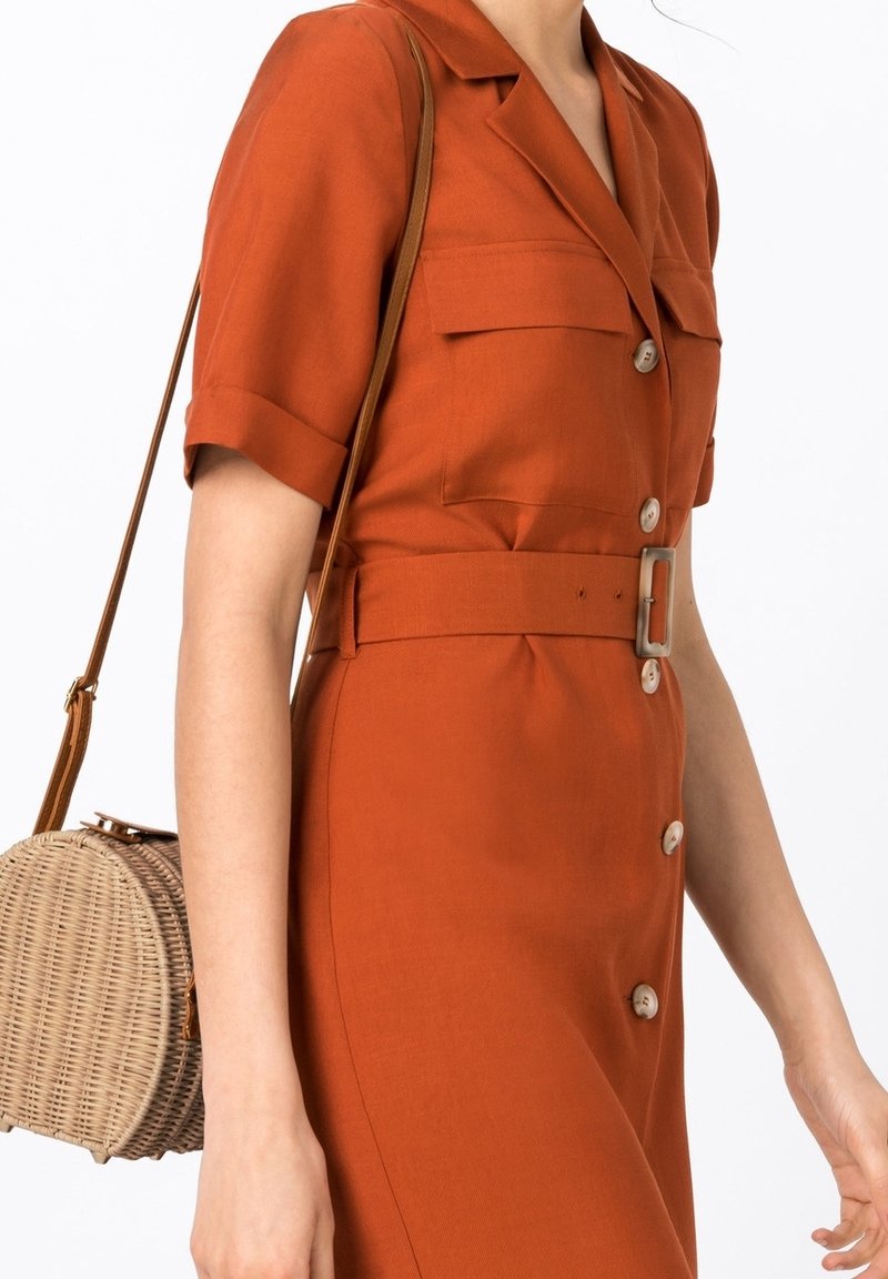 Ruskonsin väriöltämärttys mekko, jossa on lyhyet hihat, nappikiinnitys ja vyötärölle sidottu vyö. Kudottu pyöreä käsilaukku, jossa on beige olkahihna.