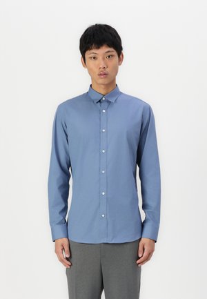 Chemise bleu à manches longues avec col, fabriquée en tissu lisse. Présente un design ajusté et des boutons blancs sur le devant.