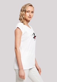 Weißes Baumwoll-T-Shirt mit kurzen Ärmeln, featuring einen schwarzen und roten Mickey Mouse Druck auf der Vorderseite. Glatte Textur und lockere Passform.