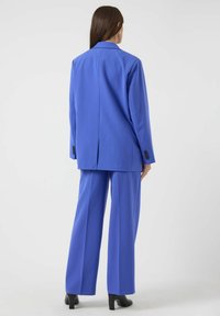 Skreddersydd blå blazer med matchende bukser med vide ben. Glatt stoff, hakket krage og svarte knappeaksenter. Minimalistisk design med en ren finish.