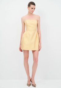 Robe jaune sans bretelles avec un motif texturé, corsage ajusté, jupe évasée et une finition lisse. Portée avec des talons pointus rehaussés d'or.