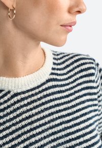 Striped sweater featuring a knit pattern in navy and white, with a soft, textured fabric and a ribbed crew neck. Gold hoop earring visible.
