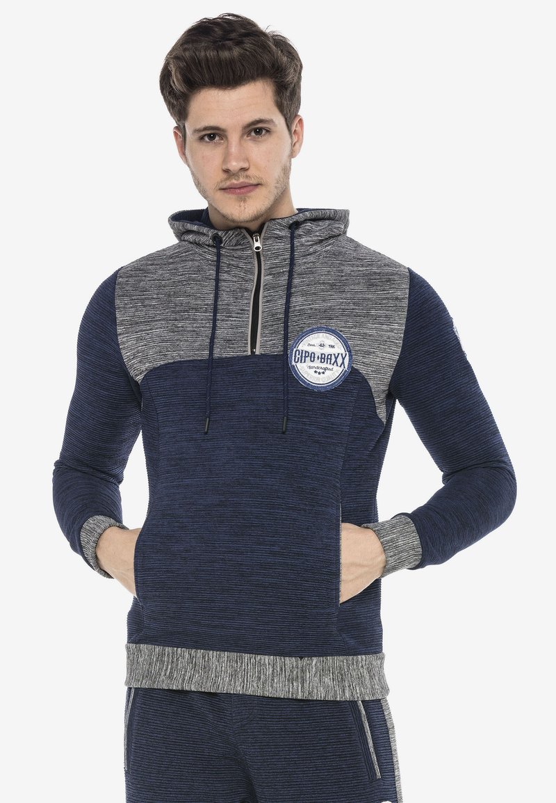 Navy- und graue Zip-Hoodie mit strukturiertem Stoff, Kängurutasche und Logo-Patch auf der Brust. Verstellbare Kordelzugkapuze.