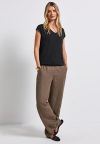 Svart kortärmad topp med V-hals, ihop med lösa, ljusbruna linnebyxor. Svarta vävda slip-on skor fulländar outfiten.