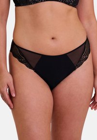 Lingerie noire avec des panneaux en maille transparente, ornée d'accents en dentelle festonnée sur les côtés, mettant en valeur un design et une texture contrastés.