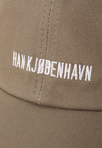 Brown cotton cap featuring white embroidered text "HAN KJØBENHAVN" on the front. Visible texture and stitching details on fabric.