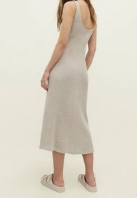 Robe midi en tricot côtelé beige avec une encolure dégagée, une silhouette ajustée et des bretelles larges, associée à des sandales compensées de couleur claire.