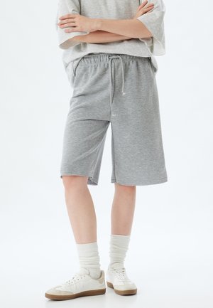 Gray cotton shorts with an elastic waistband and drawstring, featuring a relaxed fit and side slits. Paired with white sneakers and ribbed socks.