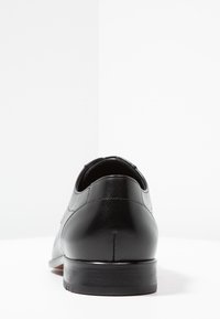 Schwarze Lederschuhe mit glatter Textur, abgerundetem Rücken und niedrigem, stabilen Absatz. Merkmale sind subtile Nähte entlang der Naht.