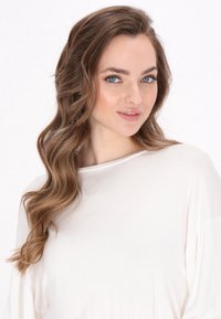 Dlouhý rukáv, lehký top z měkké bílé látky. Obsahuje široký výstřih a volný střih. Vlasy jsou vlnité, splývající přes rameno.
