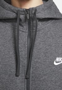 Gray zip-up hoodie, made of soft fabric, featuring a front zipper, drawstrings, and white Nike logo on the chest. Smooth texture and casual design.