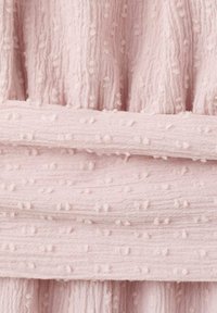 Lähikuva pehmeästä vaaleanpunaisesta kankaasta, jossa on kohokuvioituja pilkkuja ja hienovaraisia pystysuuntaisia uurteita, taitettuna kerroksittain.