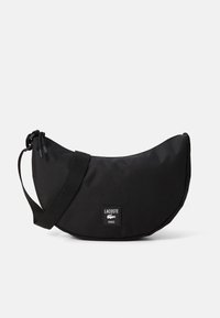 Black crescent-shaped crossbody bag with adjustable strap, zipper closure, and Lacoste Paris logo patch on front center.