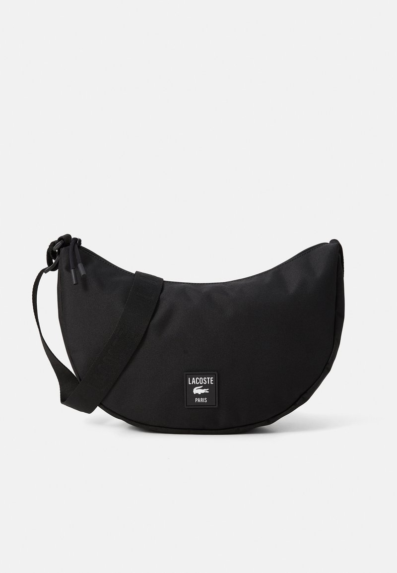 Borsa a tracolla nera a forma di mezzaluna con tracolla regolabile, chiusura con zip e patch con il logo Lacoste Paris al centro anteriore.