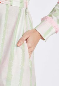 Bunt gemustertes Kleid aus leichtem Stoff mit vertikalen rosa und grünen Streifen; verfügt über eine Tasche und Rüschendetails an den Ärmeln.