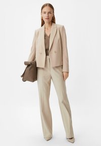 Beige, doppelt geknöpfter Blazer mit glatter Textur, kombiniert mit hellbeigen, taillierten Hosen und einer passenden Handtasche. Spitzenblick-Fußbekleidung.