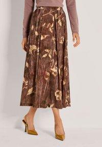 Plissé midi-jurk in bruine stof met een bloempatroon in crème en groen. Gecombineerd met gele hoge hakken. Glad textuur.