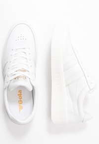 Sneakers bianchi stringati bassi con tomaia in pelle liscia, punta perforata, lacci piatti e suola in gomma texturizzata. Logo dorato sulla linguetta.