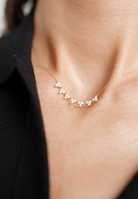 Goldkette mit fünf kleinen, dreieckigen Formen und weißen Verzierungen, vor einem dunklen Stoffhintergrund.