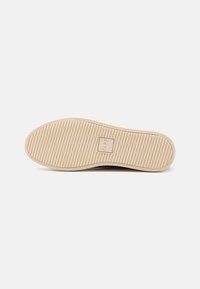 Shoe outsole with ribbed texture, in a light beige color. Features a rectangular logo stamp and a smooth edge around the perimeter.