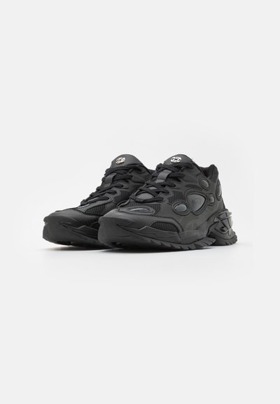Black athletic shoes featuring a textured mesh upper, rubber sole, thick cushioning, and prominent logo details on the tongue and side.