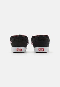 Pár čiernych tenísk Vans zobrazených zozadu s červeným a bielym logom "Off The Wall" na bielych podrážkach na jednoduchom pozadí.