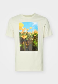 Tricou din bumbac galben deschis, cu un grafic de flori portocalii pe fond de cer albastru, având textul "Mergi cu natura." în partea de jos.