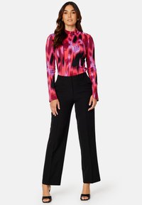 Fitted langemouwtop in een roze en zwart abstract patroon, gecombineerd met hoge zwarte wijde broekspijpen en zwarte open teen hakken.