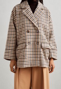 Cappotto doppiopetto realizzato in tessuto a motivo pied de poule nei toni beige, marrone e arancione, dotato di grandi tasche e maniche ampie e rilassate.