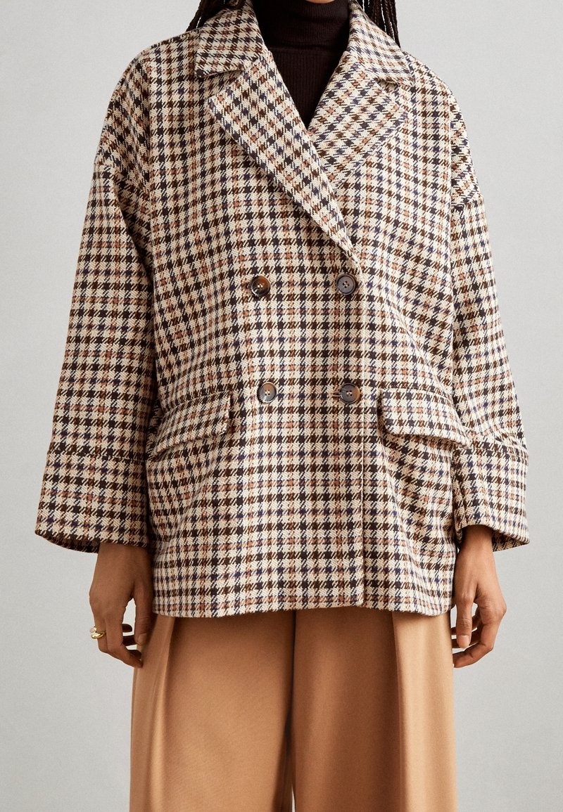 Cappotto doppiopetto realizzato in tessuto a motivo pied de poule nei toni beige, marrone e arancione, dotato di grandi tasche e maniche ampie e rilassate.