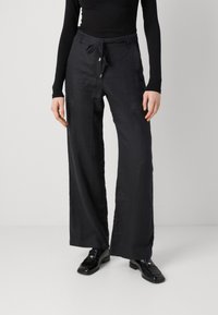 Svarta linnebyxor med vida ben och snörmidja, strukturerad yta och avslappnad passform. Kombinationen med blanksvarta loafers.