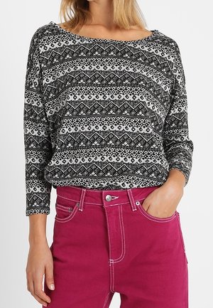 Maglione a maglia con motivo in bianco e nero, con scollatura a spalle scoperte, abbinato a jeans rosa a vita alta con cuciture a contrasto.