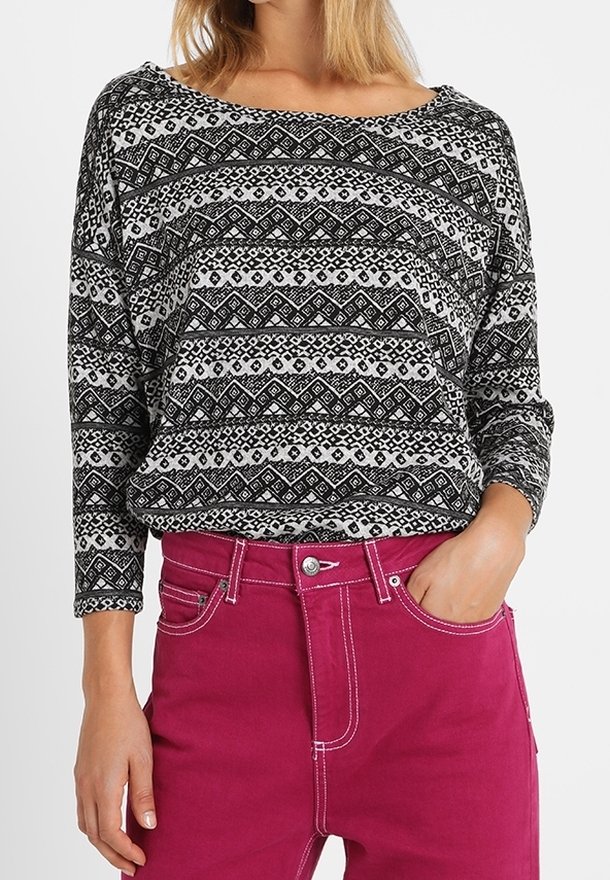 Zwart-wit gebreide trui met een off-shoulder halslijn, gecombineerd met roze hoge taille jeans met contrasterende stiksels.