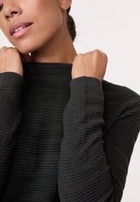 Dunkles Strickpullover mit strukturiertem, geripptem Muster. Der hohe Kragen und die schmalen Bündchen verleihen der entspannten Passform eine klare Struktur.