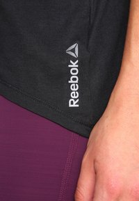 Zwart sportshirt met een grijze "Reebok" logo, gecombineerd met dieppaarse leggings. Heeft een gladde stof met nette stiksels.