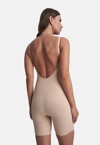 Body beige con spalline sottili regolabili, schiena bassa e taglio a pantaloncino. Presenta un'apertura funzionale sul fondo. Texture liscia.