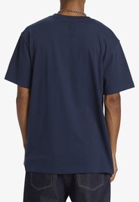 Námořnická modrá bavlněná tričko, krátké rukávy, volný střih, jednoduchý kulatý výstřih, hladká textura, bez grafik nebo vzorů, zobrazený pohled zezadu.