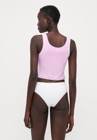 Rosa cropped tank topp med hvite detaljer, laget av et glatt stoff. Kombinert med hvite høyhalsede undertøy, som viser et minimalistisk design.
