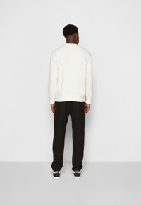 Felpa bianca con scollo rotondo, colore crema, abbinata a pantaloni neri e sneakers bianche e nere, vista da dietro.