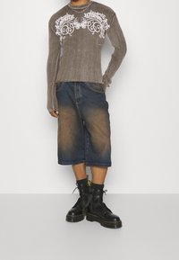 Brown ribbed long-sleeve shirt with white graphic print, paired with knee-length dark denim shorts and black lace-up boots.