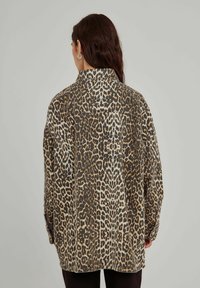 Leopardmönstrad skjorta i lättviktsmaterial, med krage, långa ärmar och knäppdetaljer, huvudsakligen i bruna, beige och svarta nyanser.