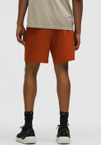 Herrers orange atletiska shorts med en lätt, slät textur; åtsittande design; sidofickor; ihop med svarta ankelsockor och skor.